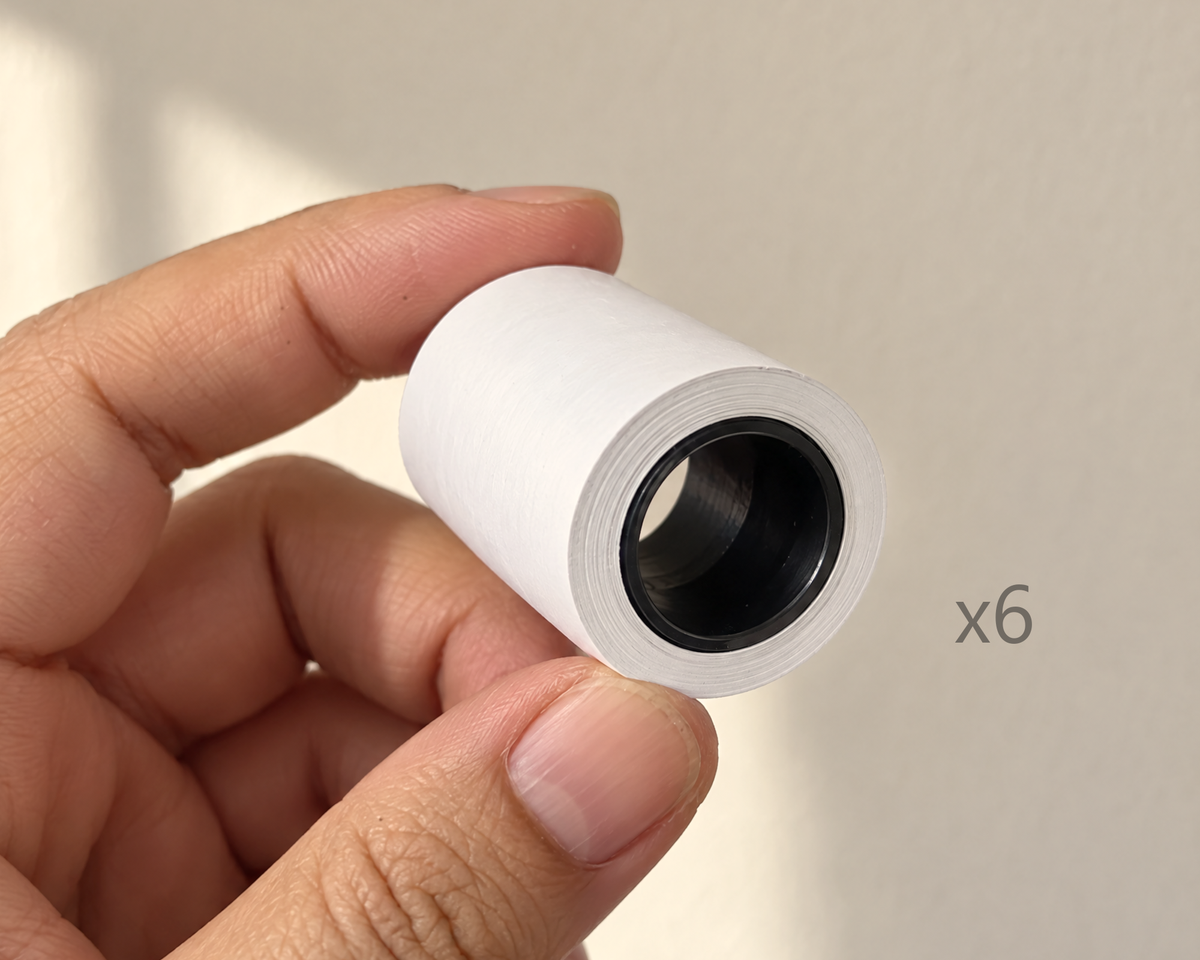 A hand holding one thermal paper roll, 40 mm wide and 27 mm across; the pack holds six